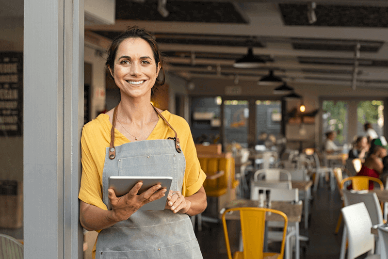 Successful small business owner in casual wearing grey apron standing at entrance